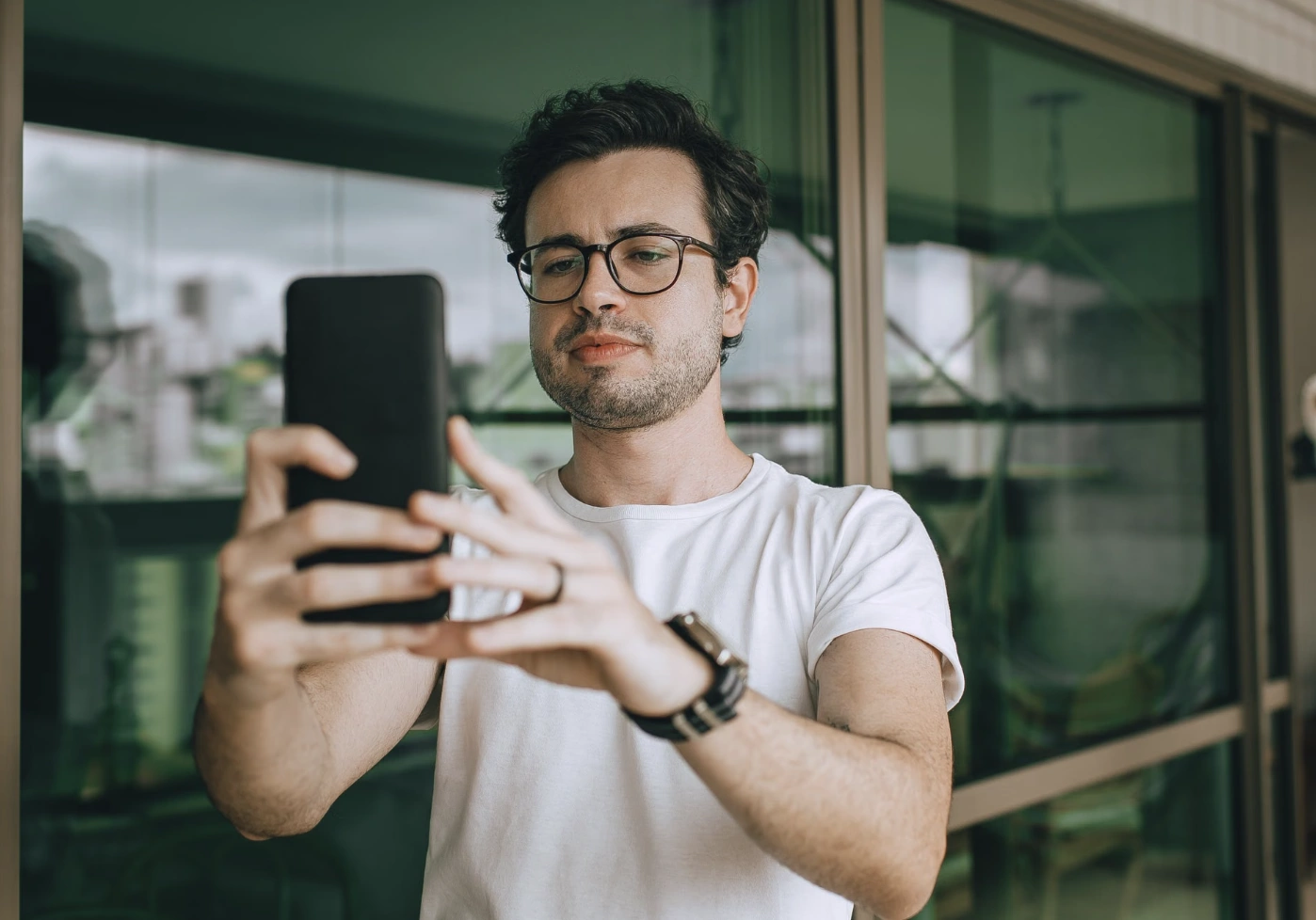 Man in glasses and a white t-shirt holding up his phone indoors